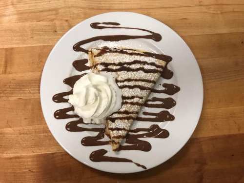 A slice of dessert topped with whipped cream and drizzled with chocolate sauce on a white plate.