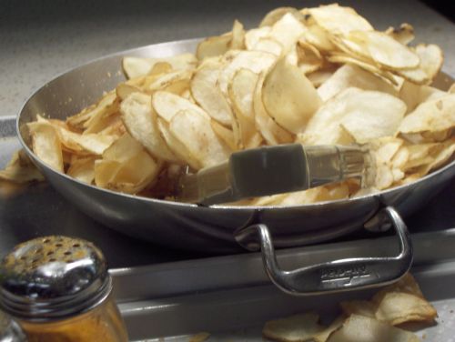 A large metal bowl filled with golden potato chips, with a serving utensil resting on top.
