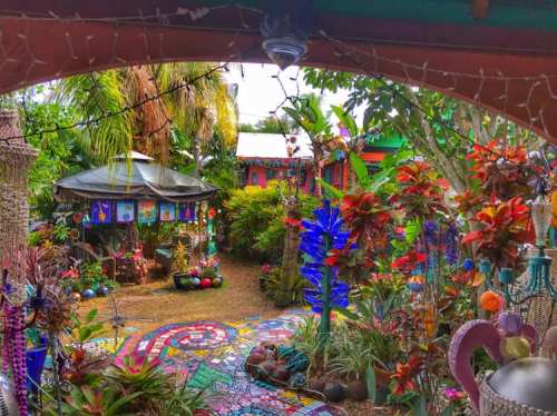 A vibrant garden filled with colorful plants, mosaic pathways, and artistic decorations under a lush canopy.