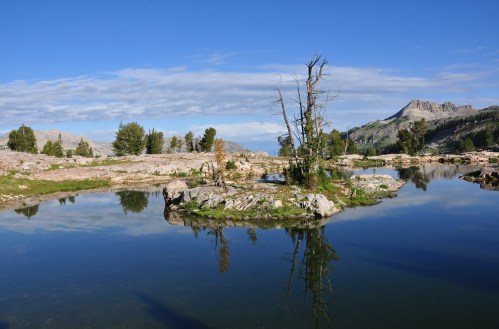 A serene landscape featuring a calm lake, rocky shore, and distant mountains under a clear blue sky.