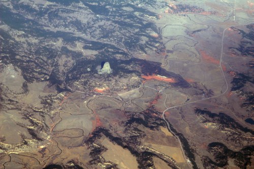 Aerial view of a mountainous landscape with winding roads and patches of red vegetation.