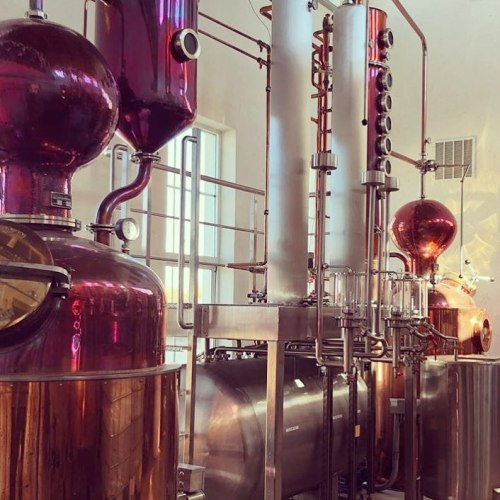 A distillation setup featuring shiny copper and stainless steel equipment in a bright, industrial space.
