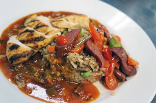 A plate of grilled chicken over rice, topped with sausage, bell peppers, and a rich tomato sauce.