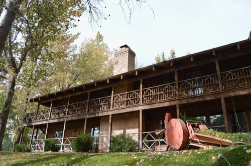A rustic wooden building with a balcony, surrounded by trees and a vintage red plow in the foreground.