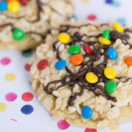 Close-up of colorful cookies topped with chocolate drizzle and candy-coated chocolate pieces on a polka dot background.
