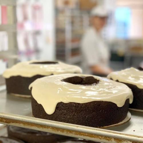 Two chocolate cakes with white icing sit on a baking tray, with a blurred figure in the background.