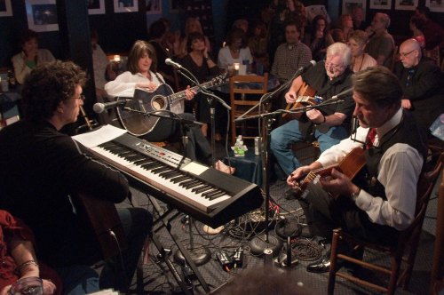 A live music performance with musicians playing guitar and keyboard in an intimate venue filled with an audience.