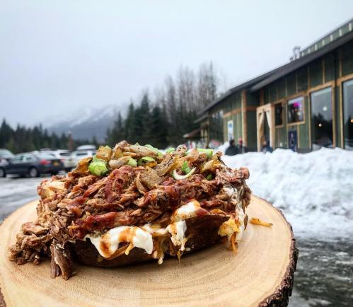 A hearty dish piled with pulled meat and toppings, served on a wooden platter, with a snowy landscape in the background.