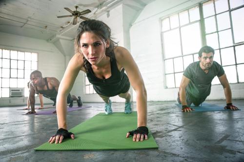 Three people doing push-ups on exercise mats in a bright, spacious room with large windows.
