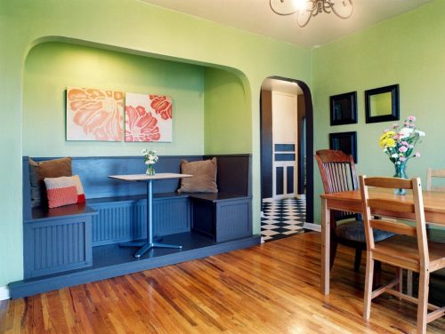Cozy dining area with a green wall, a built-in bench, a small table, and a wooden dining table with chairs.