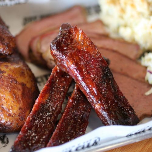 Close-up of smoked ribs and brisket on a plate, accompanied by coleslaw and a side of macaroni.
