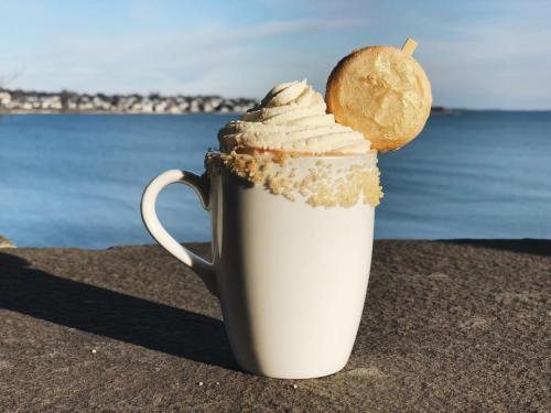 A white mug filled with whipped cream and a cookie, set against a serene waterfront background.