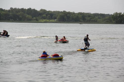 Two inflatable tubes are being towed on a lake, while a person on a paddleboard navigates nearby.