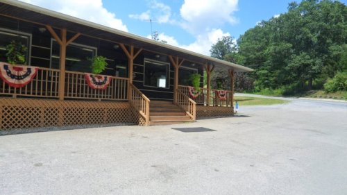 A wooden building with a porch, decorated with red, white, and blue bunting, surrounded by greenery and a clear sky.
