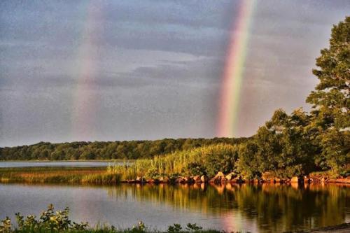 A serene lake scene with two rainbows arching over lush greenery and calm waters reflecting the sky.