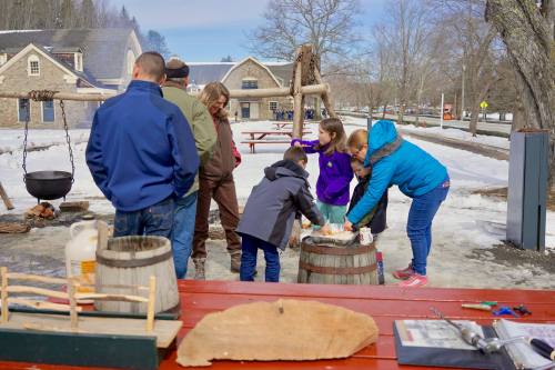 A group of people gathers around a table outdoors, engaging in a hands-on activity in a snowy setting.