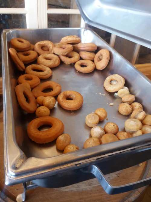 A metal tray filled with various donuts, some whole and some broken, on a wooden surface.