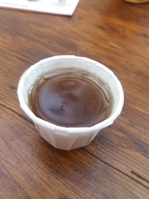 A small paper cup filled with dark liquid, resting on a wooden table.