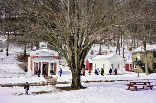 A snowy landscape with children walking near historic buildings and a large tree, creating a winter scene.