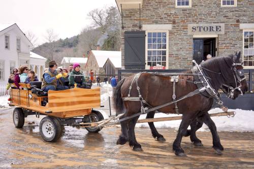 A horse-drawn wagon carries passengers through a snowy village, with historic buildings in the background.