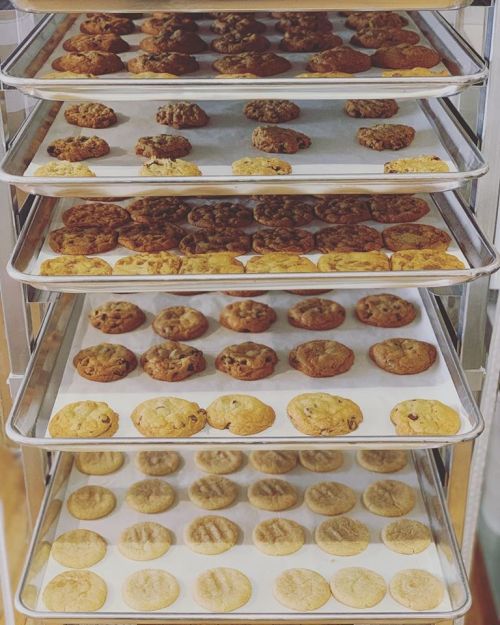 A display of freshly baked cookies on multiple trays, showcasing various types and colors.