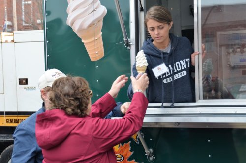 A young woman serves soft-serve ice cream from a food truck to a customer reaching out to receive it.