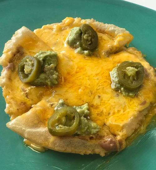 A cheesy tortilla topped with jalapeños and guacamole on a green plate.
