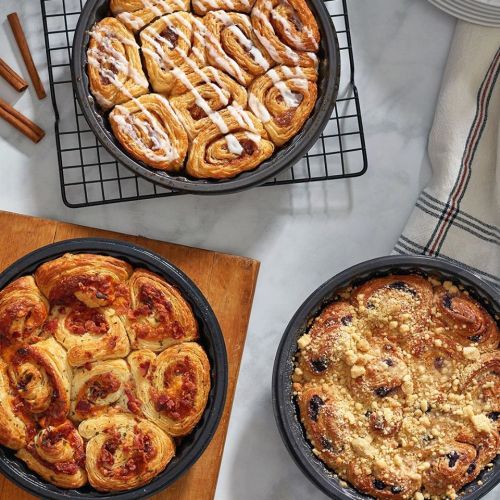Three types of freshly baked pastries: cinnamon rolls, savory rolls, and a crumb-topped sweet roll on a marble surface.