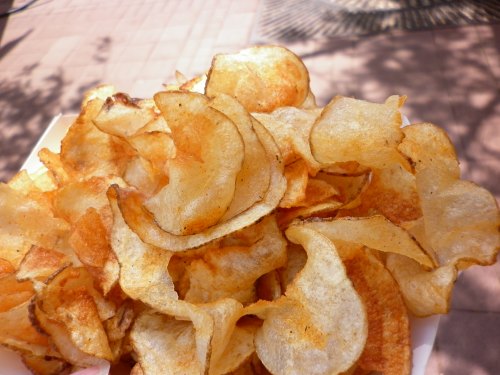 A close-up of a pile of golden, crispy potato chips on a white plate.