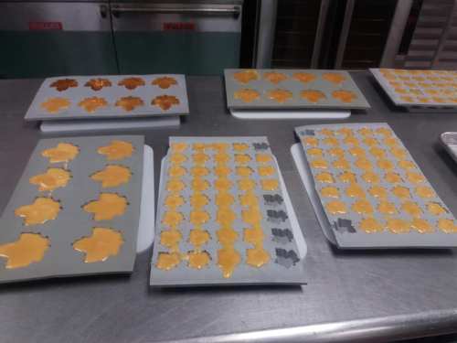 Trays of cookie dough shaped like leaves, ready for baking, on a stainless steel countertop.