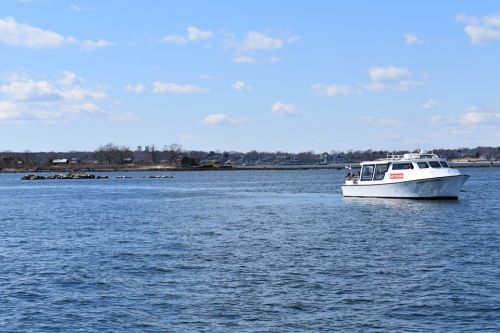 A white boat navigates through calm waters under a clear blue sky, with distant land visible in the background.