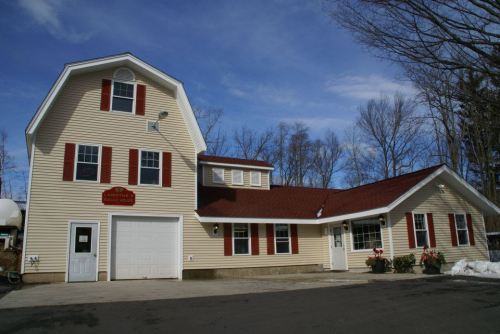 A two-story house with a red roof and white siding, featuring red shutters and a garage, surrounded by trees.