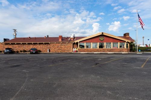 A rustic restaurant with a stone exterior and large windows, set against a blue sky with scattered clouds.