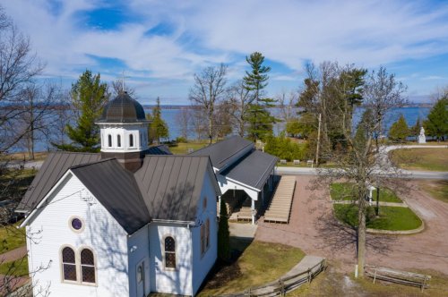 Aerial view of a white church by a lake, surrounded by trees and a clear blue sky.