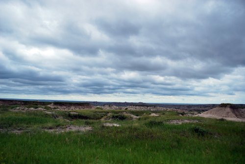 A vast landscape featuring grassy plains and rugged hills under a cloudy sky.
