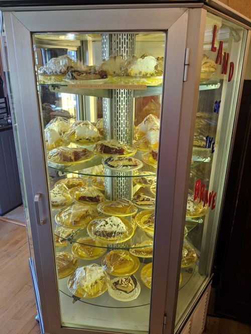 A glass display case filled with various pies and desserts, labeled "Land of the Brave."