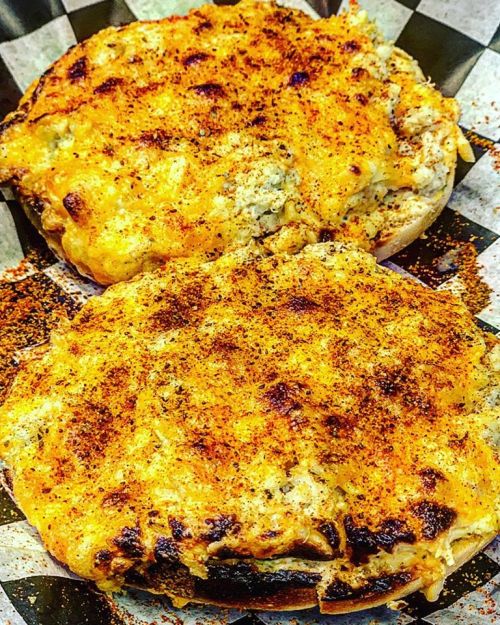 Two toasted bagels topped with melted cheese and spices, served on a checkered paper.