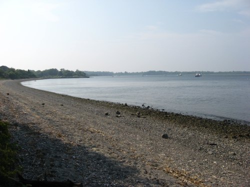 A serene beach scene with a curved shoreline, calm water, and distant trees under a hazy sky.