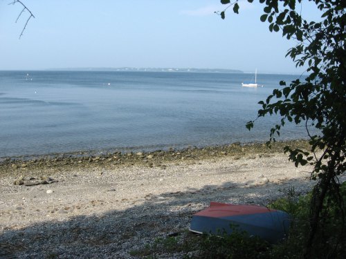 A calm shoreline with a small boat on the water, surrounded by trees and distant land in the background.