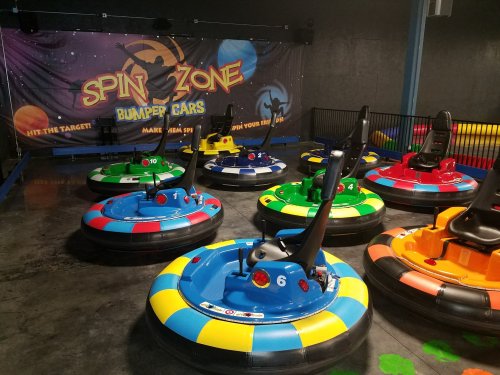 Colorful bumper cars arranged in a fun indoor arena with a "Spin Zone" banner in the background.