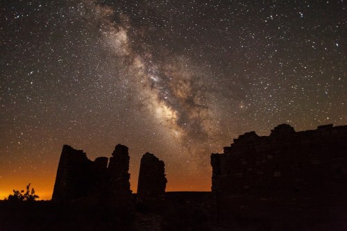 Silhouetted ruins under a starry sky, featuring the Milky Way and a warm glow on the horizon.