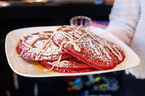 A plate of red velvet pancakes drizzled with cream cheese icing and dusted with powdered sugar.