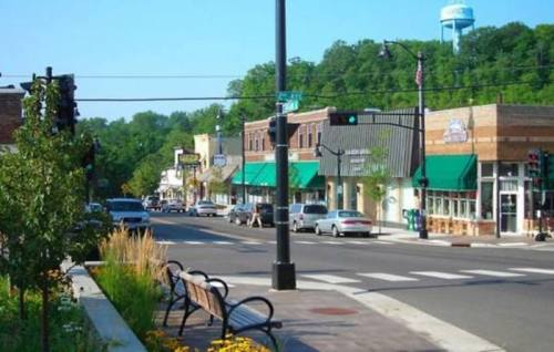 A charming small-town street with shops, greenery, and a water tower in the background on a sunny day.