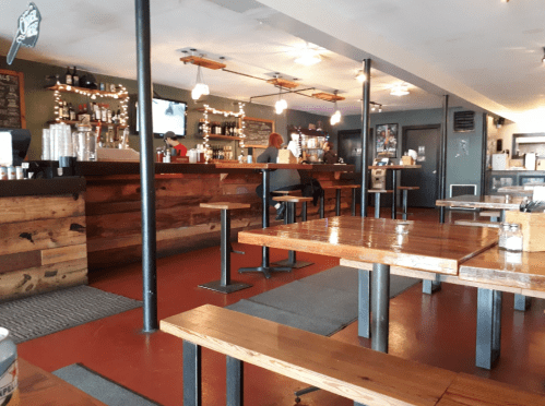 Interior of a cozy bar with wooden tables, a long counter, and warm lighting, featuring a few patrons and a relaxed atmosphere.