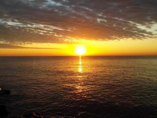 A serene sunset over calm waters, with vibrant orange and yellow hues reflecting on the surface.