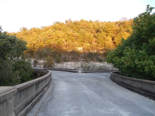 A winding road curves through a landscape of trees with autumn foliage, leading towards a hillside.