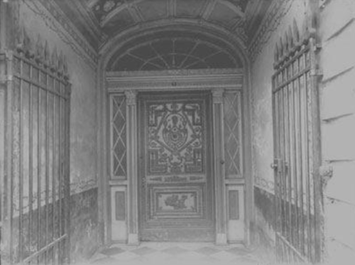 A vintage entrance with an ornate wooden door and wrought iron gates, featuring intricate designs and a weathered appearance.
