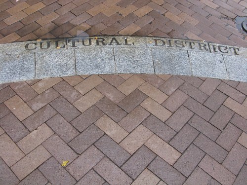 A stone pathway with the words "Cultural District" engraved, set in a pattern of brown and gray bricks.