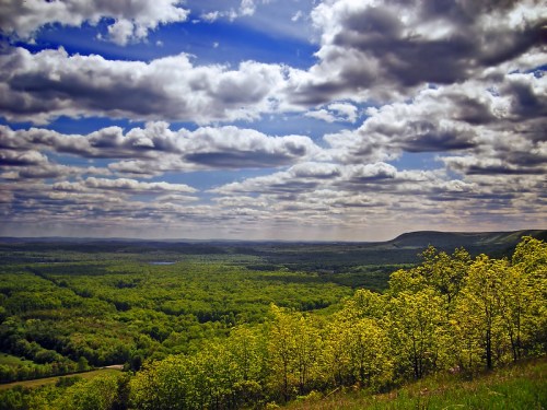 A panoramic view of lush green hills under a bright blue sky filled with fluffy clouds.