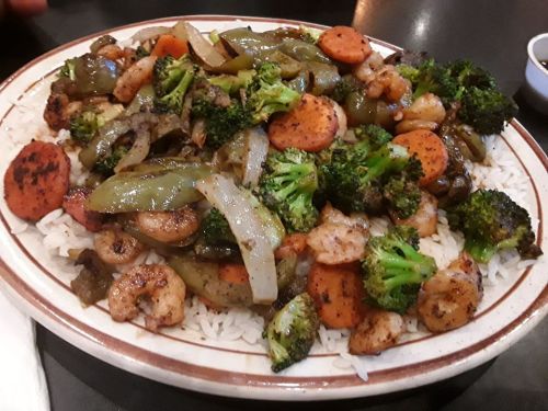 A plate of stir-fried shrimp and vegetables, including broccoli, carrots, and bell peppers, served over rice.